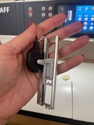 Person holding a sewing machine accessory in front of a sewing machine.
