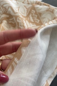 Person holding fabric with intricate beige patterns on a white background.
